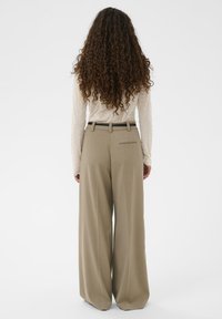 Platie zilbju bikses gaiši bēšā audumā ar gludu faktūru, priekšpusē ar krokām un aizmugurē ar kabatu, kopā ar krēmkrāsas rakstainu garām piedurknēm topu.