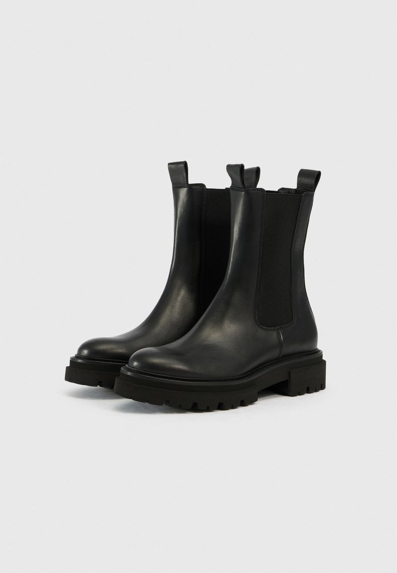 Bottines Chelsea en cuir noir avec des panneaux élastiques sur les côtés, des languettes de traction et des semelles crantées épaisses sur fond uni.