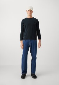 Czarna koszula z długim rękawem, niebieskie dżinsy, czarne tenisówki i biała czapka; prosty design, dopasowany fason u góry, luźne spodnie o prostych nogawkach.