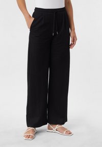 Black wide-leg pants made from soft fabric with an elastic waistband and drawstring. Features side pockets and a relaxed fit. Paired with white sandals.
