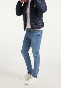 Veste matelassée marine, t-shirt blanc, jean skinny bleu clair et baskets blanches. La veste comprend une fermeture éclair et un détail logo.