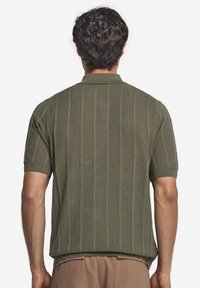 Kortärmad, texturerad polo med olivgrön färg. Har vertikal ribbad design, smal krage och åtsittande ärmslut.