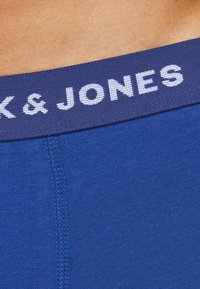 Blaue Stretchstoff-Boxershorts mit einem dunkelblauen elastischen Bund, der den weißen Text "JACK & JONES" zeigt. Glatte Textur und kontrastierende Nähte.