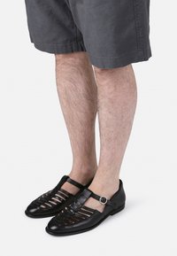 Mustat nahkasaappaat, joissa on leikattuja muotoja, soljella varustettu hihna ja tasapohja. Yhdistetty harmaisiin shortseihin.