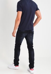 Mörk denimjeans med smal passform, kombinerade med en marinblå t-shirt. Vita sneakers med röda accenter fulländar outfiten. Inga synliga mönster eller logotyper.