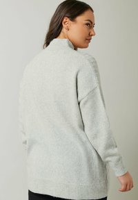 Lichtgrijze gebreide trui met een hoge kraag, relaxte pasvorm en geribbelde manchetten, met een subtiele textuur en zijsplitten voor extra comfort.
