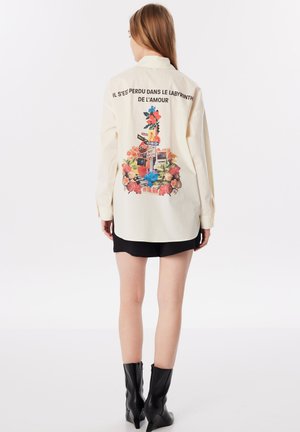 Long-sleeve cream shirt with vibrant floral and graphic print on back; includes text in French and decorative elements.