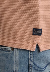 Svetle růžová texturovaná košile s detailem v zakončení, se modrou etiketou "Petrol Ind", v kombinaci s modrými džíny.