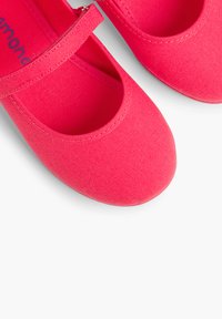 Balerini din pânză roz, cu vârful rotund și o curea peste glezna piciorului, având un material texturat și detalii de cusătură în contrast.