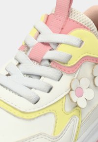 Λευκό αθλητικό παπούτσι με ροζ και κίτρινες λεπτομέρειες, υφασμένα κορδόνια και λουλουδάτη διακόσμηση με ροζ κέντρο. Λείο συνθετικό υλικό.