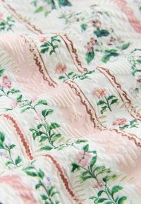 Tissu matelassé doux avec des motifs floraux roses, verts et marron disposés en sections carrées sur un fond blanc.