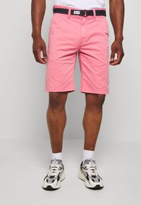 Rosa bomullsshorts med ett svart bälte, med en klassisk skärning och sidfickor. Bärs med gråa och vita sneakers och vita strumpor.