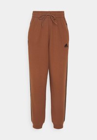Brown Adidas jogger pants with elastic waistband, drawstring, side pockets, black Adidas logo, and black stripes along legs.