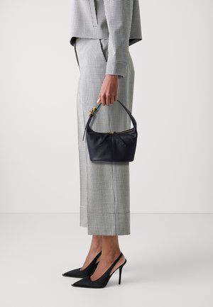 Small black leather handbag with a curved top handle and a gold zipper, paired with a checkered gray and white outfit and black pointed heels.
