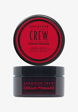 Zwart potje van American Crew Cream Pomade met een rood label waarop licht vasthouden en lage glans staat, afgebeeld met het deksel boven het potje op een witte achtergrond.