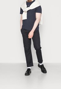 Námořnické tričko s kulatým výstřihem, krémový svetr přehozený přes ramena, černé zúžené kalhoty a černé boty s hladkým povrchem.