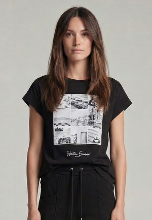 Woman with long brown hair wearing a black t-shirt featuring a black-and-white photo collage and black pants with drawstrings.