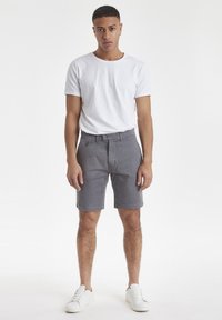 Pantalones cortos de algodón grises con corte recto, pasadores para cinturón y bolsillos laterales, combinados con una camiseta básica blanca de cuello redondo y zapatillas blancas.