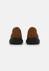 Bruine suède schoenen met een ronde neus, voorzien van een zwarte rubberen zool en een gestructureerde grip. Eenvoudig ontwerp zonder extra versieringen.