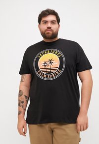 Sort bomulds T-shirt med et cirkulært grafisk motiv af palmer og teksten "JACK & JONES PALM SPRING" i gule og hvide nuancer.