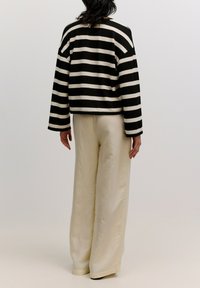 Zwart-wit gestreepte gebreide jas met een cropped silhouet, gecombineerd met crèmekleurige wijde broekspijpen. Gladde textuur en een ontspannen pasvorm.