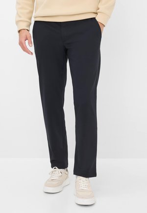 Marineblauwe tapered broek van lichte stof, met zijzakken en een gladde afwerking, gecombineerd met beige sneakers.