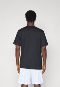 T-shirt noir �à manches courtes en coton, avec un col rond et une coupe décontractée, associé à un short de sportif blanc.