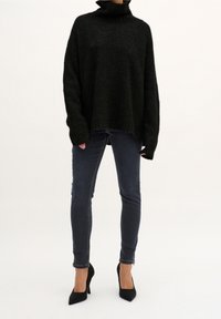 Suéter negro de punto oversized con cuello alto, combinado con jeans ajustados azul oscuro y tacones negros de punta.