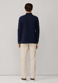 Granatowa polo z długim rękawem i kołnierzykiem, z zapięciem na guziki, w połączeniu z beżowymi spodniami i brązowymi, niskimi trampkami. Prosty i nowoczesny design.