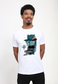 Camiseta blanca de algodón con un diseño impreso de un edificio estilizado con acentos en azul verdoso y naranja, graffiti y salpicaduras de color.