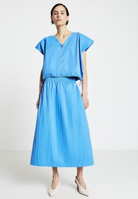 Vêtement léger bleu avec encolure en V et manches courtes. Taille élastique et jupe fluide arrivant à mi-mollet. Texture lisse.