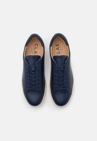 Zapatillas de piel vegana azul marino con textura suave, punta redonda y suela de goma blanca. Cuenta con cierre de cordones y logo en relieve.