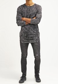 Maglia grigia a maniche lunghe con motivo marmorizzato e scollo rotondo, abbinata a jeans skinny neri con dettagli a costine e strappi, indossata con sneakers nere.