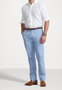 Ljusblå bomullsbukser i kombination med en vit linneskjorta, brunt läderbälte och bruna mockaloofer, med en minimalistisk design.