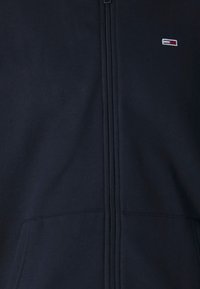 Sudadera con cremallera en color navy, fabricada en una mezcla de algodón, con detalles de costura vertical y un pequeño logotipo en el lado izquierdo del pecho.