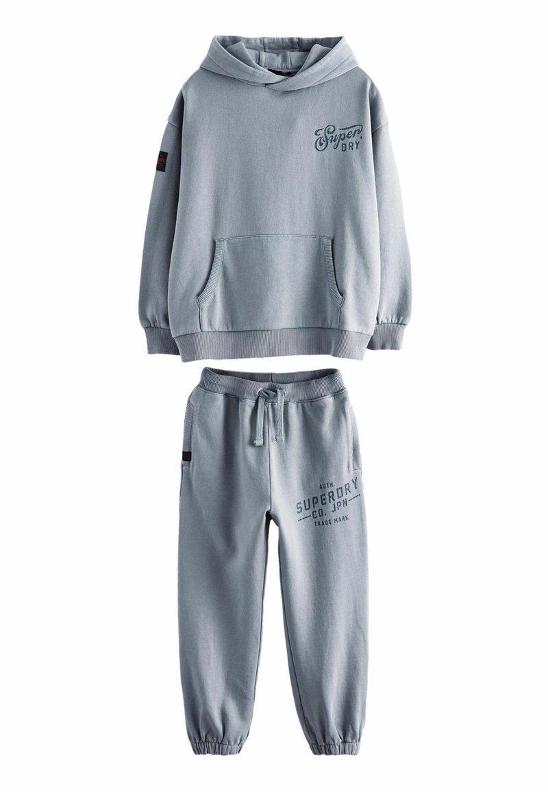 Sættet i lyseblåt bomulds loungewear indeholder en hættebluse med en lommer foran og tilhørende tætsiddende bukser med elastisk talje og trykt logo.