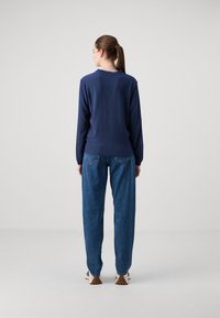 Marineblå langermet teksturert topp med rund hals, kombinert med lyseblå rette jeans og lyse sneakers.