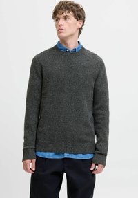 Pull gris charbon avec un col rond et des poignets côtelés, fabriqué à partir d'un tissu texturé, superposé sur une chemise bleu clair.