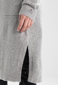 Grå ulltröja med ribbade mudd, sidoflikar och en liten logodetalj. Mjuk textur, lång ärm och avslappnad passform.