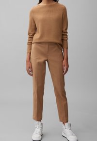 Beżowy sweter dzianinowy z długimi rękawami, zestawiony z beżowymi spodniami od garnituru. Całość dopełniają białe sneakersy z wysoką cholewką. Prosty i nowoczesny design.