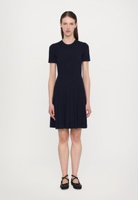 Navy ribbed dress with a short sleeve and round neckline, featuring a flared skirt and pleated design, paired with black ballet flats.