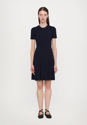 Navy ribbed dress with a short sleeve and round neckline, featuring a flared skirt and pleated design, paired with black ballet flats.