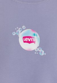 Tissu violet avec un groupe de bulles iridescentes entourant une grande bulle affichant le logo Levi's en blanc et rouge.