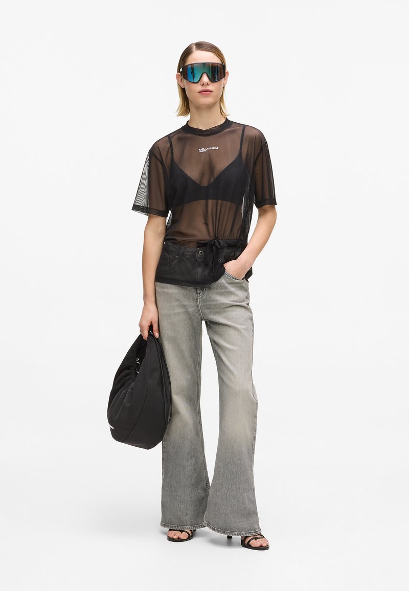 Tricou negru transparent cu mâneci scurte, blugi gri cu picior larg, geantă neagră și ochelari de soare supradimensionați cu lentile reflectorizante. Textul de pe tricou este vizibil.