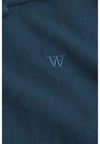 Polo de culoare bleu marin, cu o textură moale din bumbac, având un mic logo brodat "W" într-o nuanță mai deschisă pe piept.