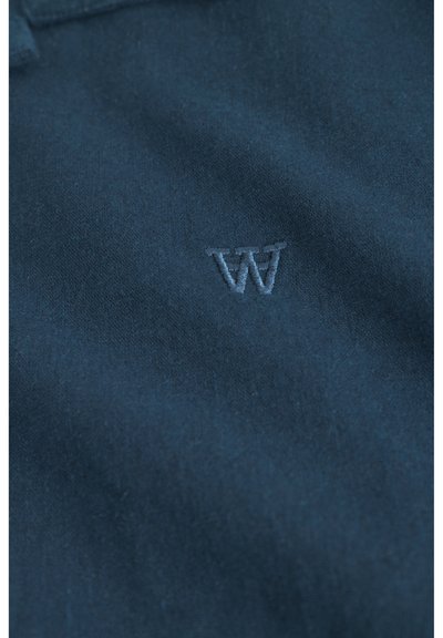 Námornícky modrá polokošeľa s jemnou bavlnenou textúrou a malým vyšitým logom "W" v svetlejšej farbe na hrudi.