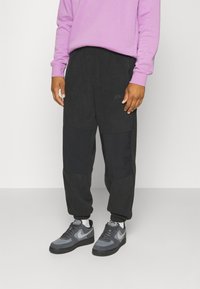 Černé jogger kalhoty se strukturovaným povrchem, vybavené bočními zipovými kapsami a logem Nike. Doplněné šedými teniskami a fialovou mikinou.