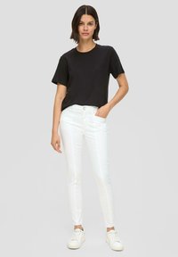 Schwarzes kurzärmliges T-Shirt kombiniert mit weißen Slim-Fit-Jeans und weißen Sneakers. Das Outfit zeichnet sich durch ein schlichtes Design und klare Linien aus.