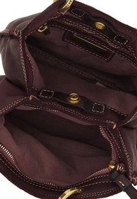 Interno di una borsa in pelle bordeaux con accessori dorati, tasche con zip e cuciture a contrasto. Fodera in tessuto morbido visibile.