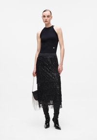 Black sleeveless top with textured neckline paired with a black fringed sequin skirt. Sheer black boots and small handbag.